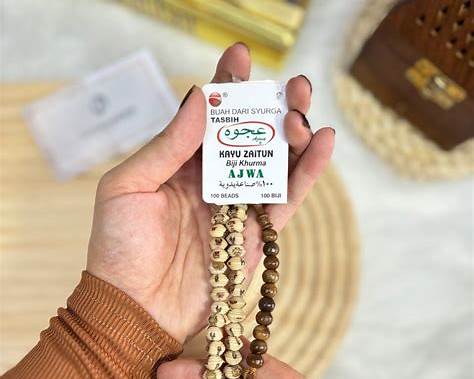 Tasbih dari biji kurma (date seed tasbih) dengan butiran alami berwarna cokelat dan krem, ditampilkan dalam genggaman tangan sebagai perlengkapan ibadah dzikir.